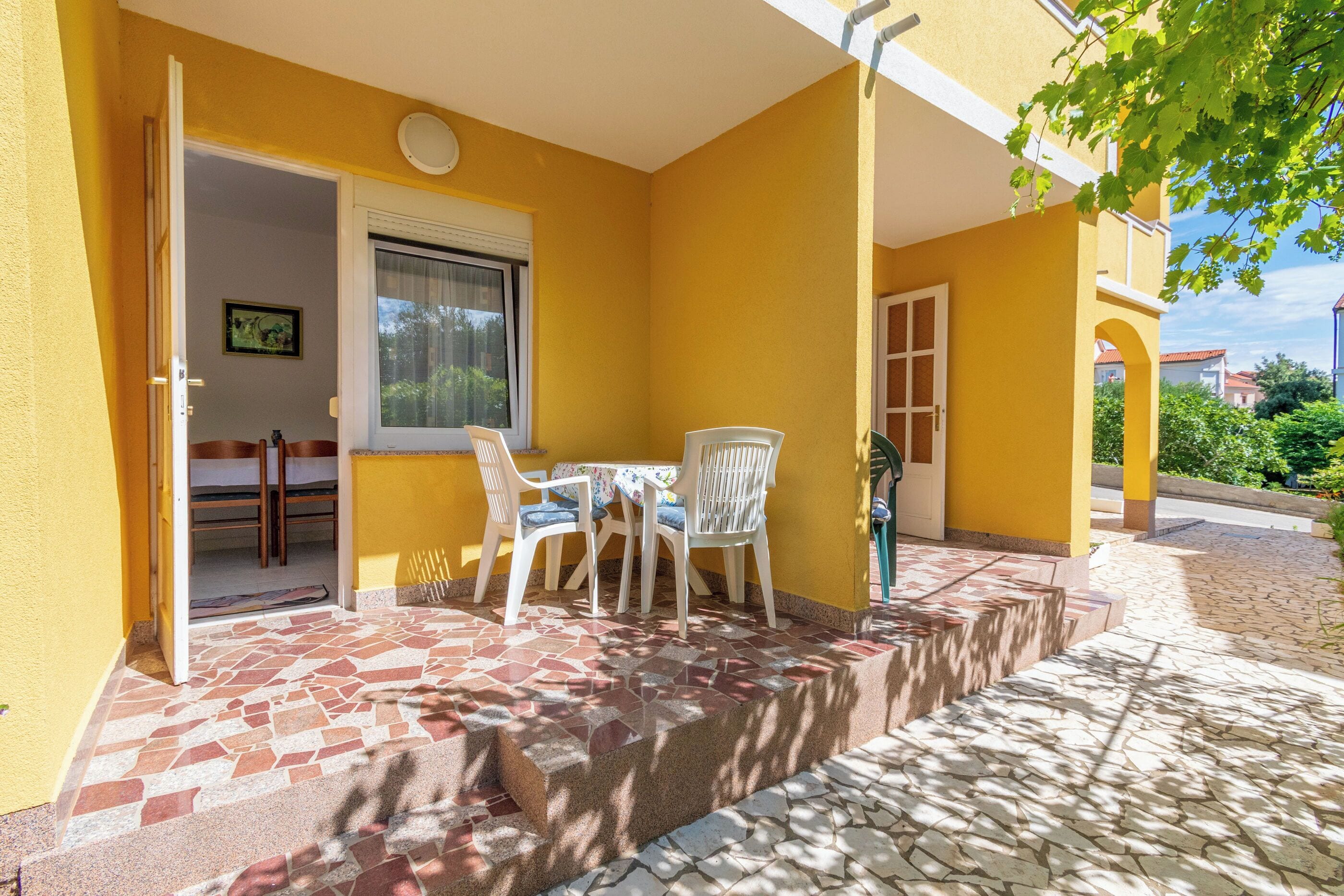 A yellow building with a patio area featuring a tiled floor, a table with chairs, and a door leading to an interior room.
