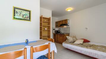 A compact room with a dining table, chairs, a bed, a kitchen area, and a framed picture on the wall.