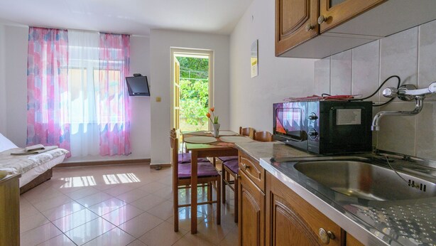 Una cocina con microondas, pileta, armarios de madera, una mesa de comedor con sillas y una ventana con cortinas.
