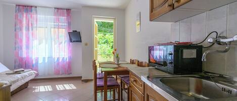 A kitchen with a microwave, sink, wooden cabinets, a dining table with chairs, and a window with curtains.
