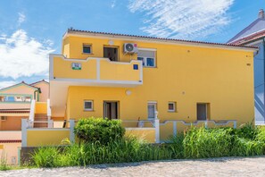 A yellow two-story building with balconies, a small window, and a door. - Apartments Tomo (Lopar)