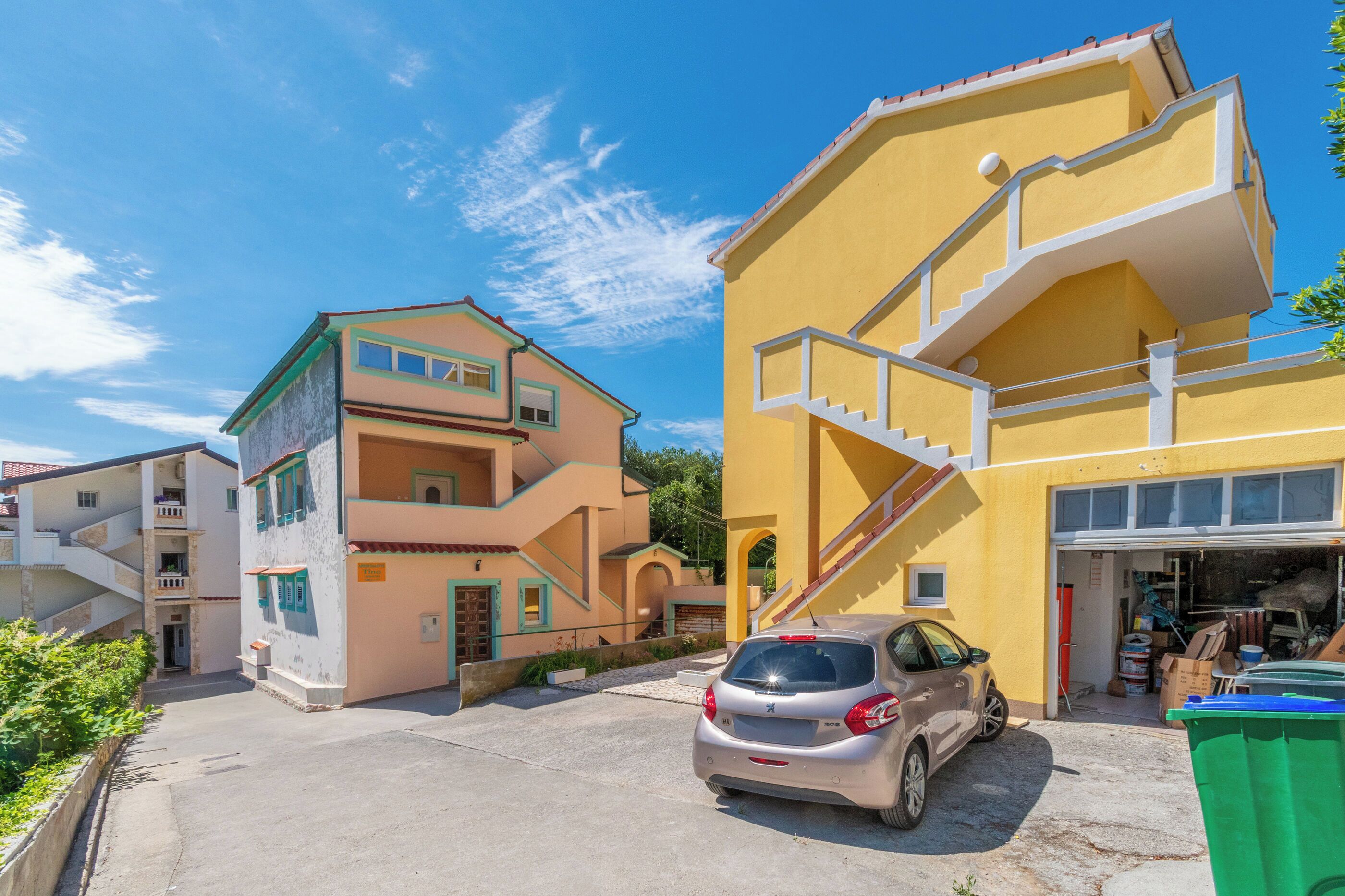 Un quartier résidentiel avec des immeubles à plusieurs étages, une voiture garée devant et un garage où sont entreposés divers objets.