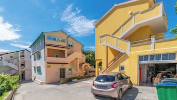 Zona residencial com edifícios altos, um carro estacionado na frente e uma garagem com objetos guardados.