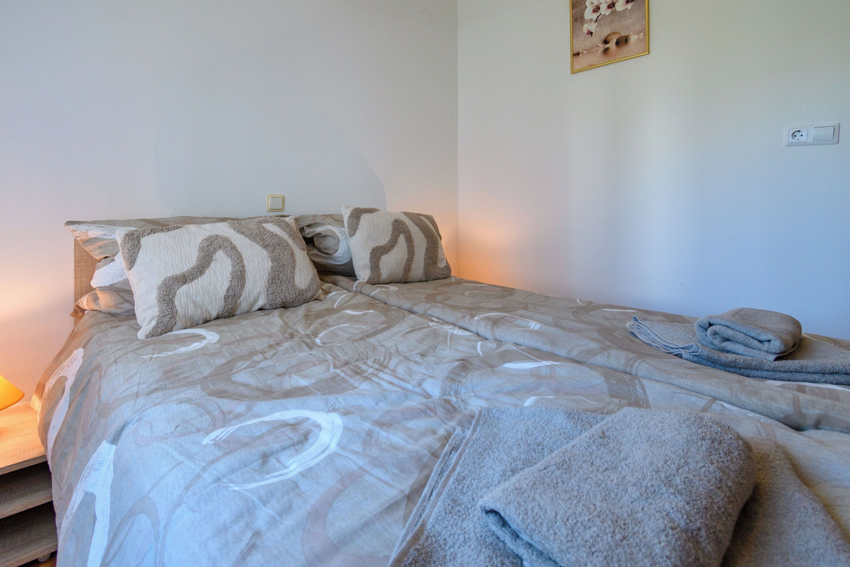 Cama bem arrumada com roupa de cama estampada e uma toalha enrolada ao lado.