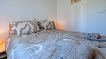 Cama bem arrumada com roupa de cama estampada e uma toalha enrolada ao lado.