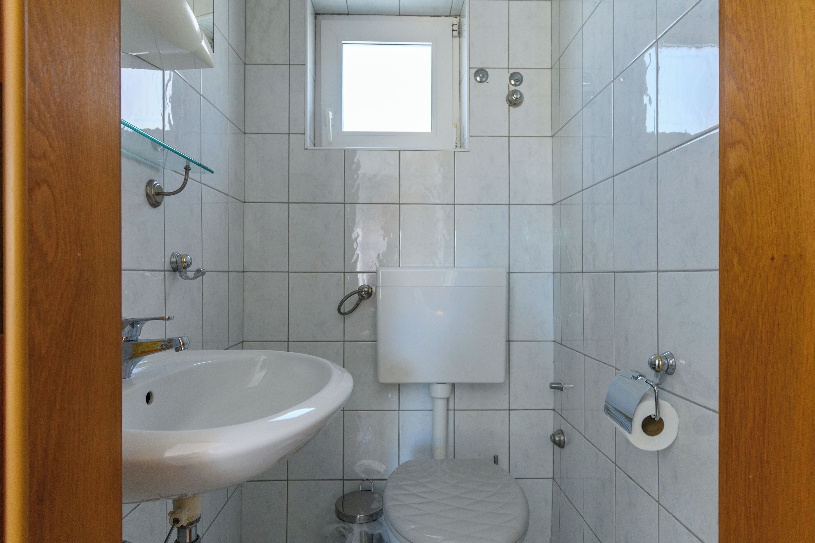 A bathroom with a sink, toilet, and a small window above the toilet.