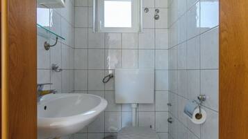 A bathroom with a sink, toilet, and a small window above the toilet.
