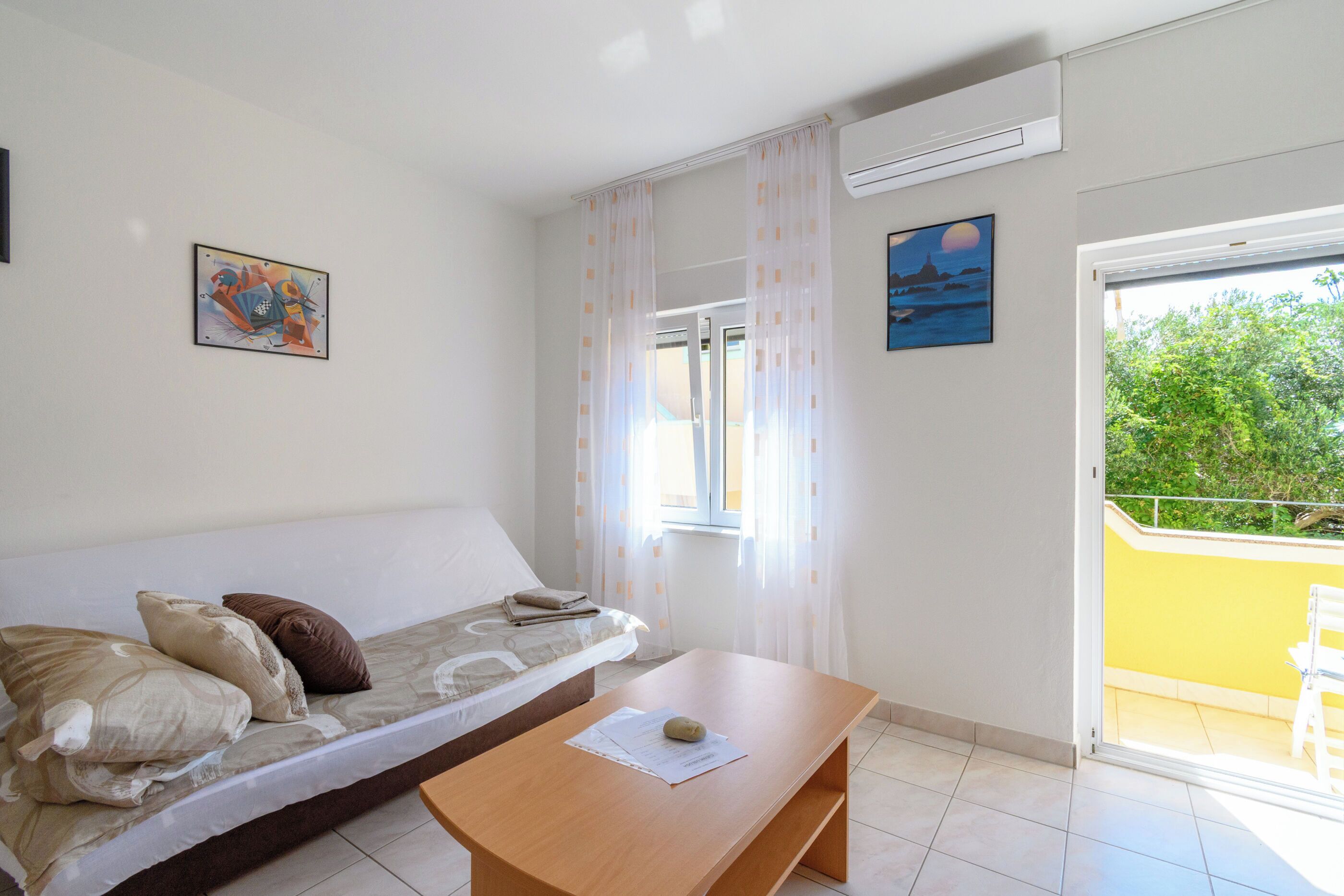 Una habitación con cama, una mesa, un ventanal con cortinas y un balcón con barandilla.
