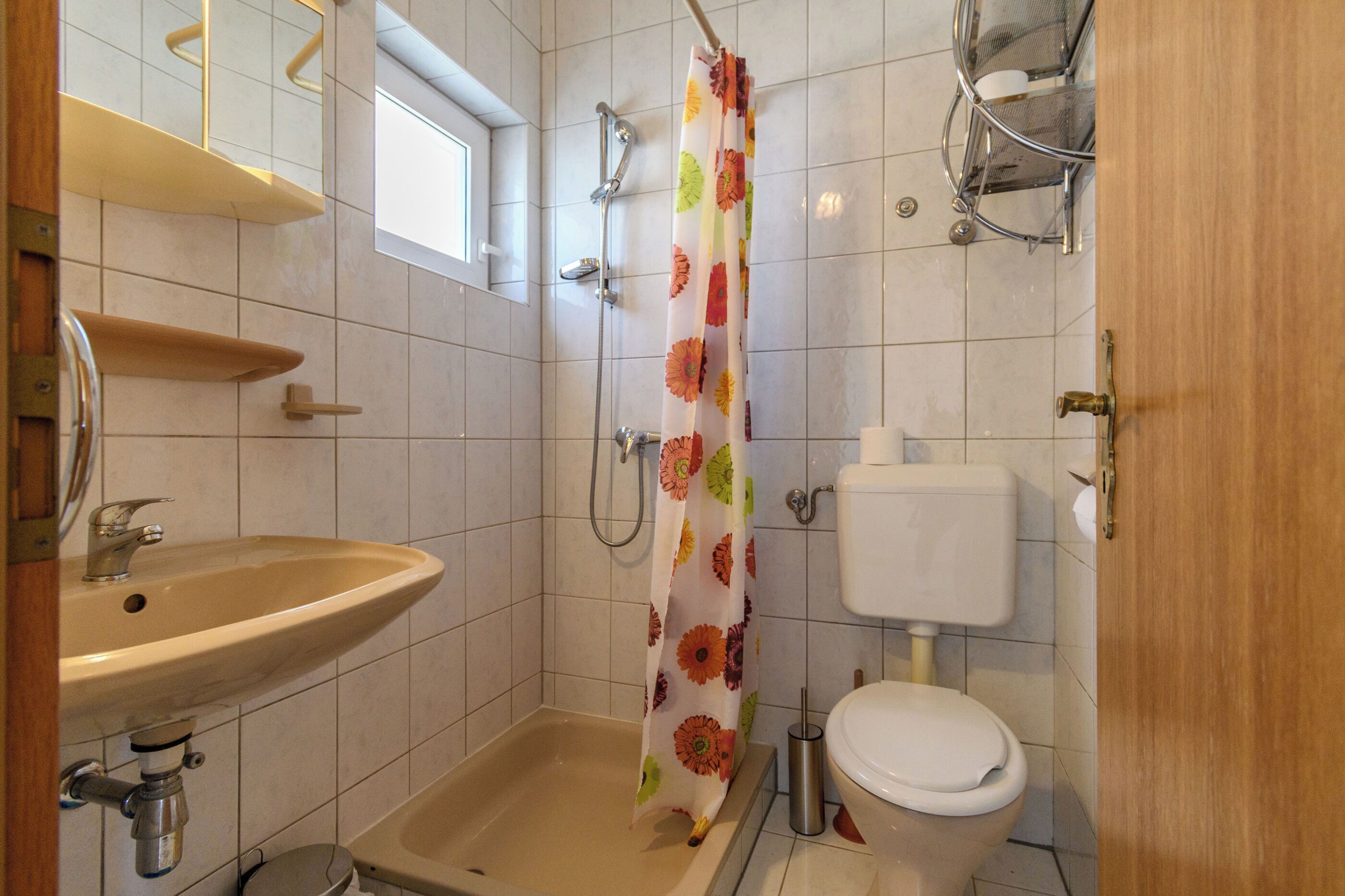 A bathroom with a sink, toilet, shower, and a window.