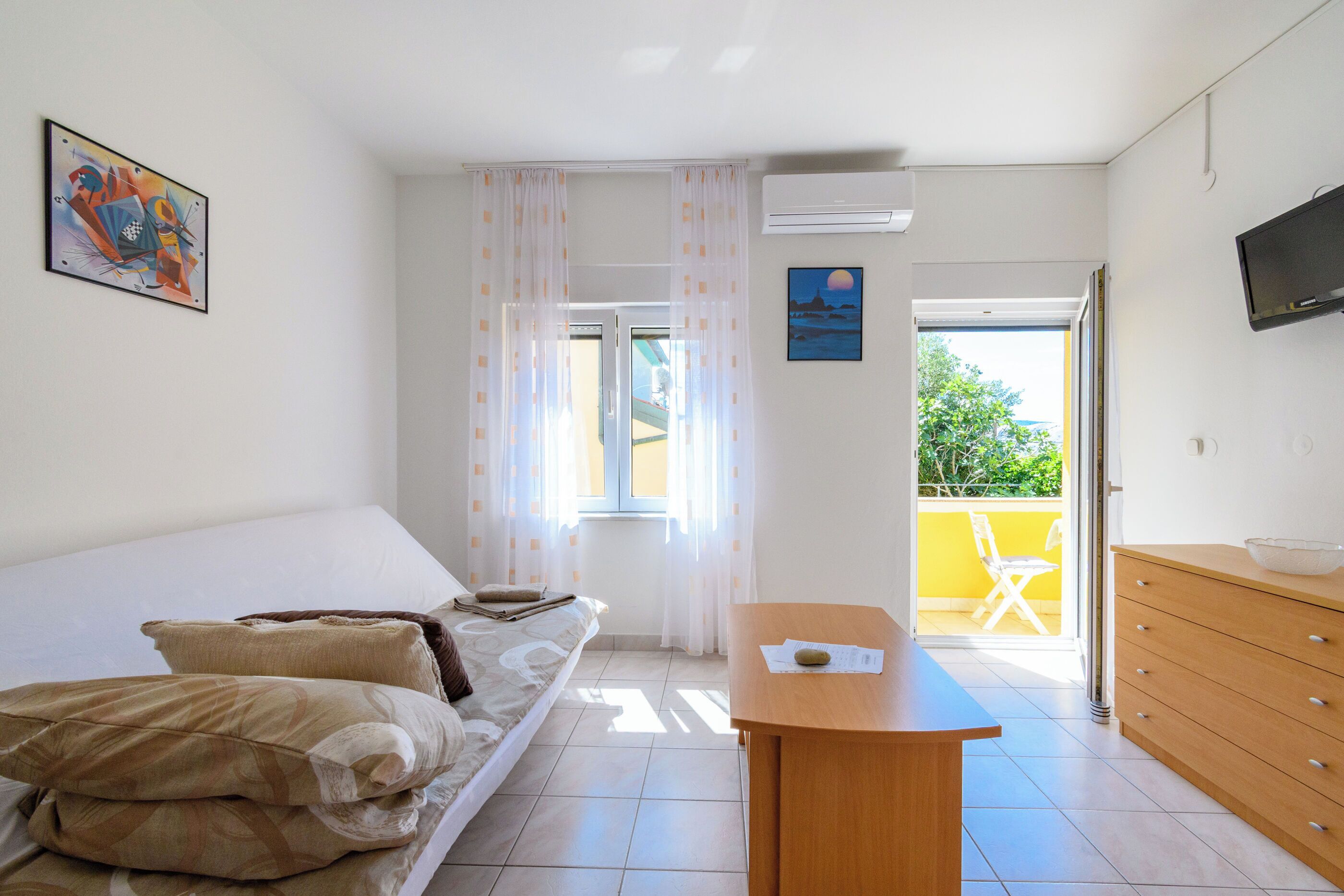 Une chambre à coucher avec un lit, une commode en bois, un téléviseur et une fenêtre avec des rideaux.