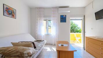 Une chambre à coucher avec un lit, une commode en bois, un téléviseur et une fenêtre avec des rideaux.