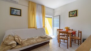 Una habitación con un sofá, una mesa de comedor con sillas, un ventanal con cortinas amarillas y dos cuadros en las paredes.