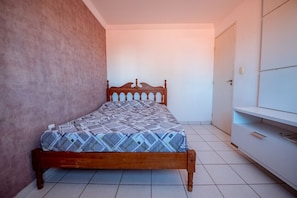 A bedroom with a wooden bed, a white wardrobe, and a tiled floor.