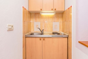 A compact kitchen with a sink, a stove, and wooden cabinets. - Apartments Branko (Dugi Rat)