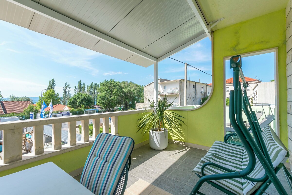 A balcony with a view of buildings, a potted plant, and striped chairs.