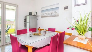 A dining area with a glass table, pink chairs, a refrigerator, a painting, and a potted plant. - Apartments Branko (Dugi Rat)