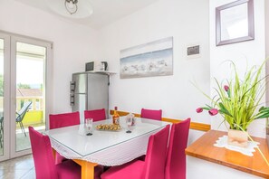 A dining area with a glass table, pink chairs, a refrigerator, a painting, and a potted plant. - Apartments Branko (Dugi Rat)