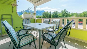 A balcony with a table and chairs, a view of mountains, and a green wall. - Apartments Branko (Dugi Rat)