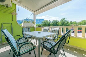 A balcony with a table and chairs, a view of mountains, and a green wall. - Apartments Branko (Dugi Rat)