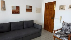 Een woonkamer met een grijze bank, een fauteuil met patroon en een houten deur.