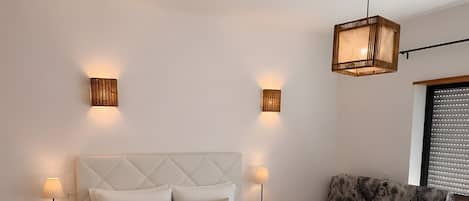 A bedroom with a bed, bedside tables, a sofa, and a hanging light fixture.