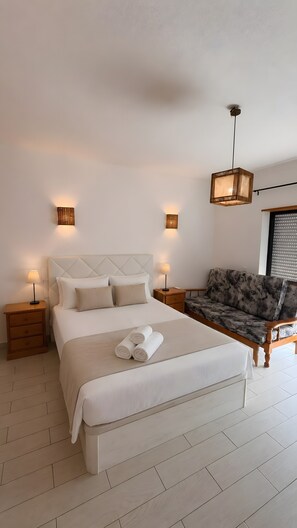 A bedroom with a bed, bedside tables, a sofa, and a hanging light fixture. - Apartment 'Cozy  in Montechoro' with Balcony, Wi-Fi and Air Conditioning (Albufeira)