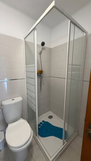 A bathroom with a glass-enclosed shower, a toilet, and a blue bath mat. - Apartment 'Cozy  in Montechoro' with Balcony, Wi-Fi and Air Conditioning (Albufeira)