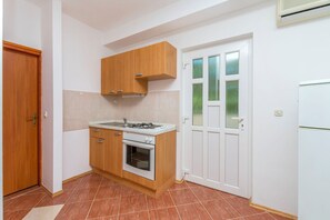 Une cuisine de taille réduite, équipée d’une cuisinière à gaz, d’un four, de meubles en bois et d’un réfrigérateur blanc.