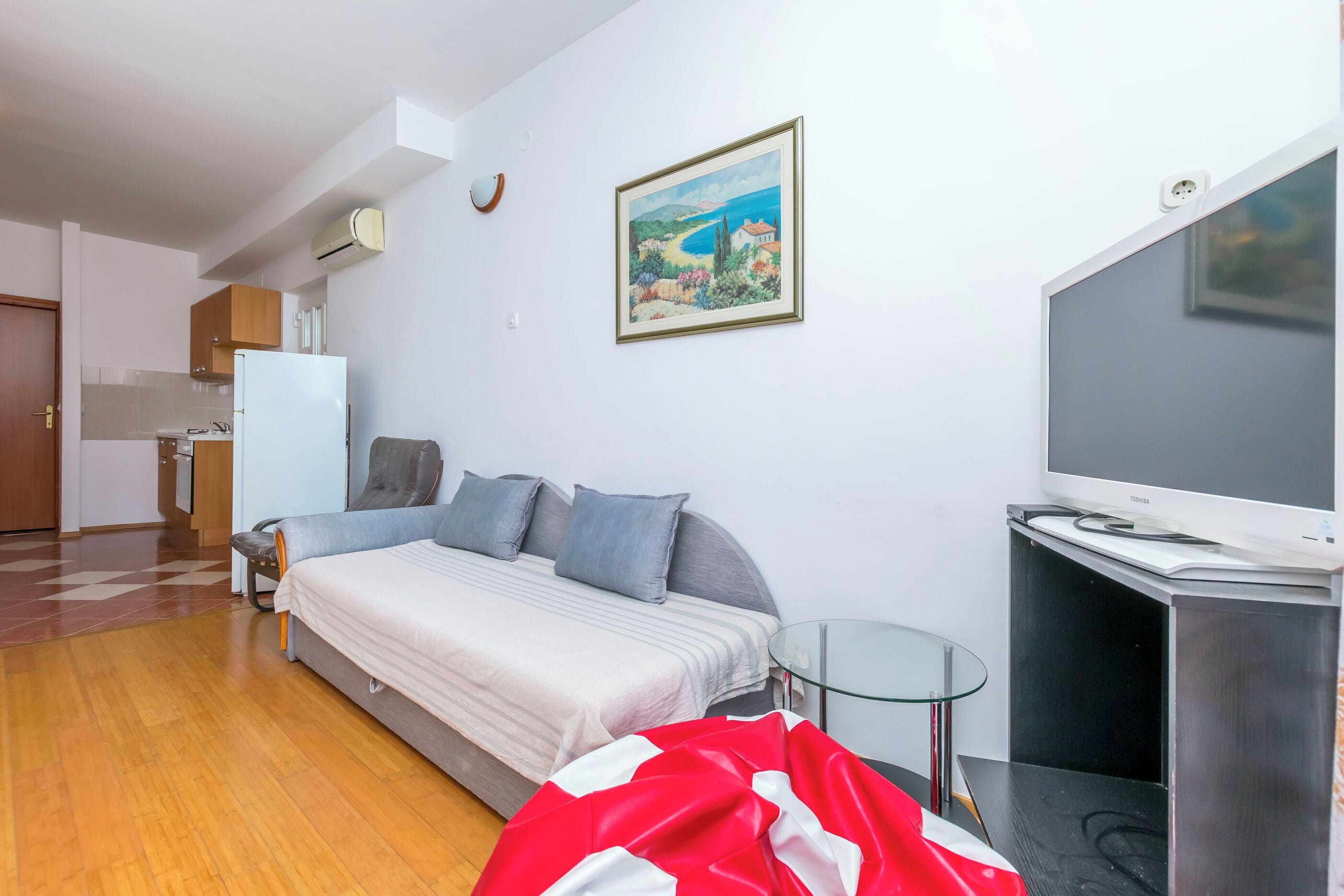 Quarto com uma cama, televisão, mesa de vidro e um quadro na parede.