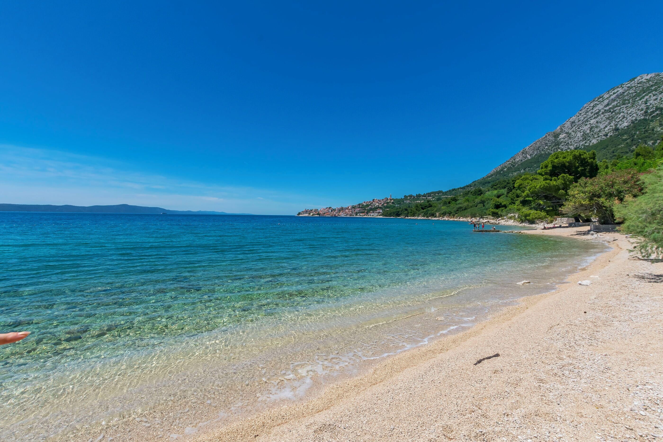 Una playa con agua cristalina, una orilla arenosa y montañas al fondo.