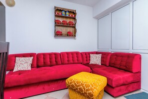 Een rode modulaire bank met twee bijpassende kussens, een geel voetenbankje en een houten plank met rode borden en decoratieve objecten.