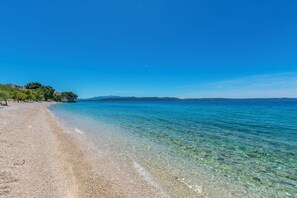 Une plage propre, bordée de galets, une mer calme et des montagnes qui se dessinent à l’horizon.