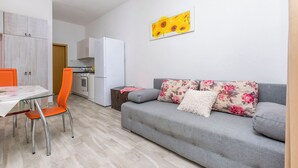 A modern living room with a grey sofa, orange chair, and a dining table with a glass top. - Apartments Zeljana on the Beach (Podgora)
