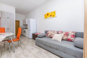 Ein modernes Wohnzimmer mit grauem Sofa, einem orangefarbenen Sessel und einem Esstisch mit Glasplatte.