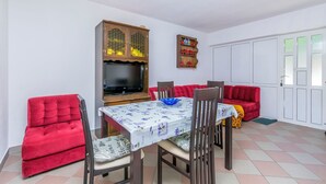 A dining area with a table, chairs, a sofa, a cabinet, and a television. - Apartments Zeljana on the Beach (Podgora)