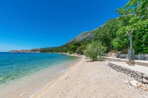 Ein Strand mit klarem Wasser, einer Steinmauer und einem Metallpfosten.