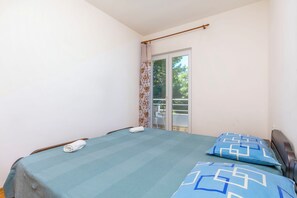 Ein Schlafzimmer mit einem Bett, zwei Kissen, einem Fenster und einer Tür, die auf einen Balkon führt.