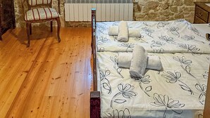 A bedroom with a stone wall, a wooden chair, a radiator, a bed with floral bedding, and a window with curtains. - House Stancija Bursic (Marcana)