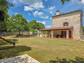A stone building with a tiled roof, a covered patio with potted plants, and a stone pathway leading to the entrance. - House Stancija Bursic (Marcana)