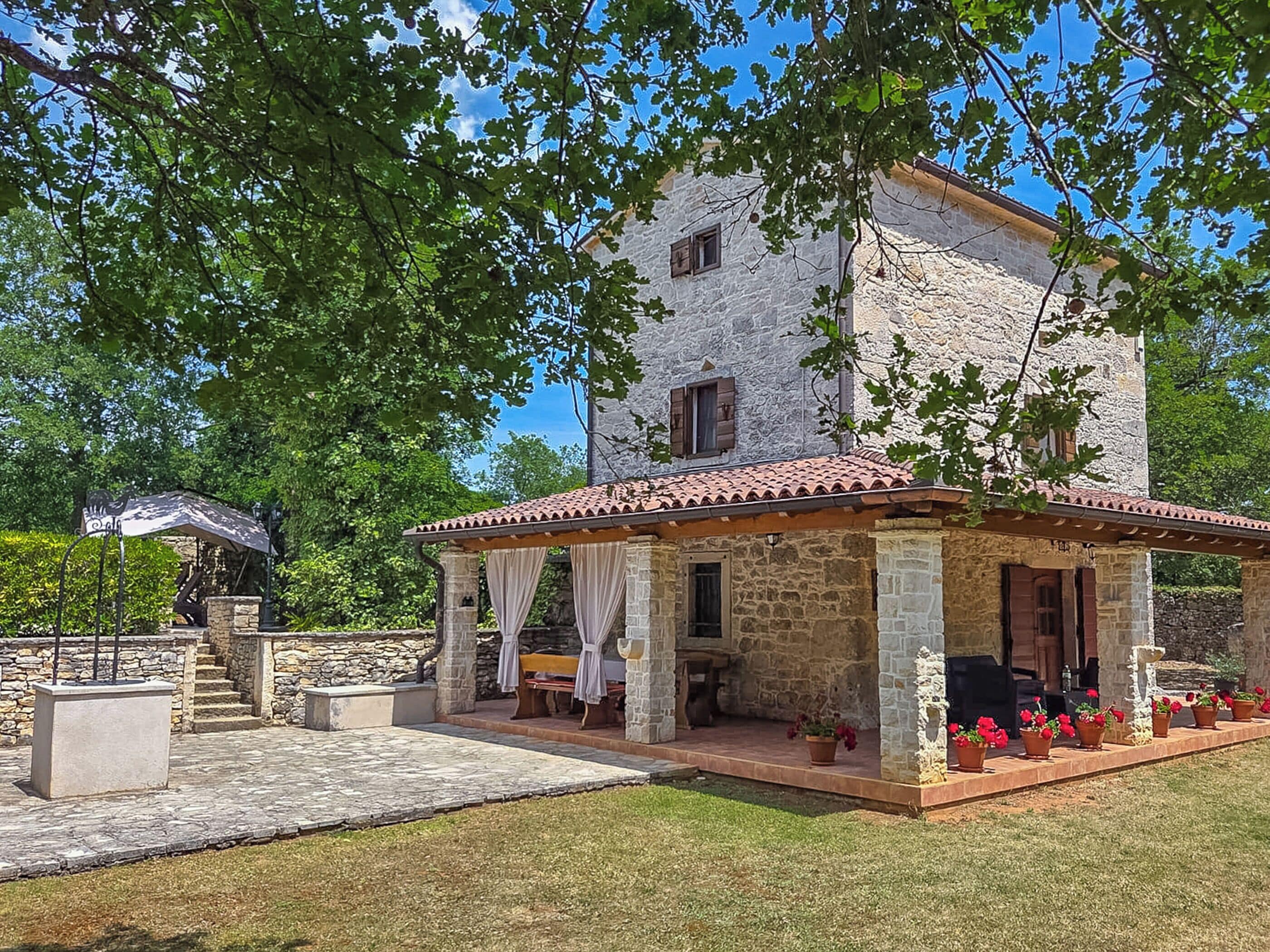 Un bâtiment en pierre avec un toit en tuiles, un patio couvert avec des sièges extérieurs et un jardin agrémenté de plantes en pot.
