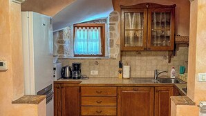 A kitchen with a central island, wooden cabinets, a built-in oven, and a window with curtains. - House Stancija Bursic (Marcana)