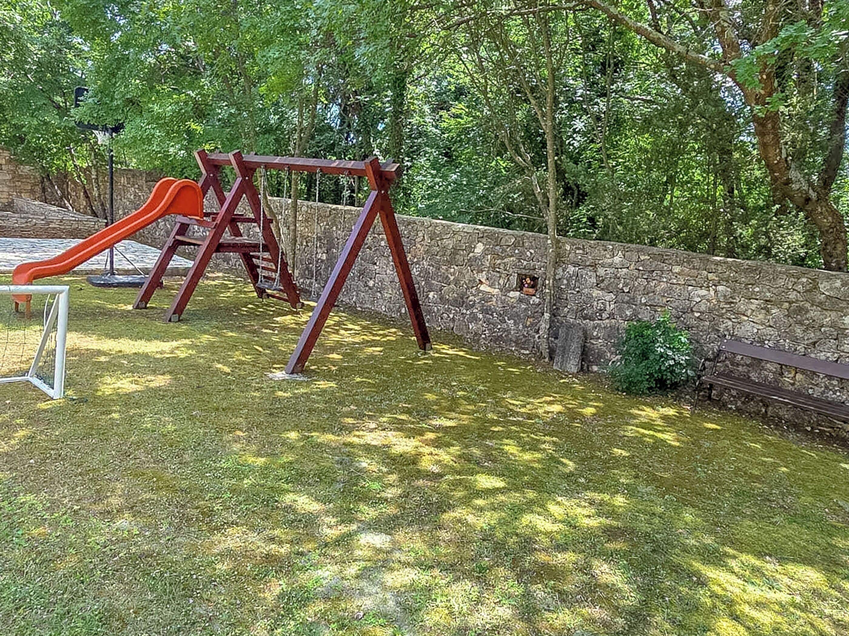 Ein Spielplatz mit Rutsche, Schaukeln, einer Steinmauer und einer Bank.