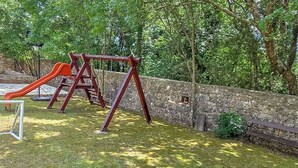 A playground with a slide and swings, a stone wall, and a bench. - House Stancija Bursic (Marcana)