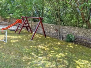 Ein Spielplatz mit Rutsche, Schaukeln, einer Steinmauer und einer Bank.