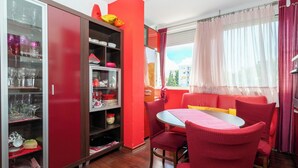 A dining area with a red table and chairs, a glass cabinet with dishes, and a window with curtains. - Apartment Near City Center (Split)