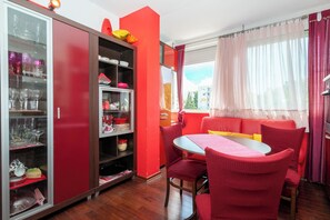 A dining area with a red table and chairs, a glass cabinet with dishes, and a window with curtains. - Apartment Near City Center (Split)