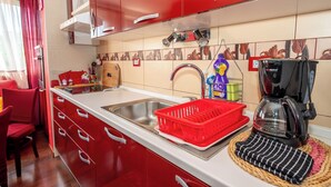A kitchen with red cabinets, a stainless steel sink, a coffee maker, and a red dish rack. - Apartment Near City Center (Split)