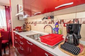 A kitchen with red cabinets, a stainless steel sink, a coffee maker, and a red dish rack. - Apartment Near City Center (Split)