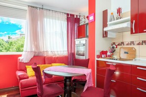 Ein rot-weißes Zimmer mit Esstisch, Stühlen, einer Couch, einer Küchenzeile und einem Fenster mit Vorhängen.