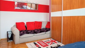 A room with a sofa, a mirror, a wooden wardrobe, and a red and white wall. - Apartment Near City Center (Split)